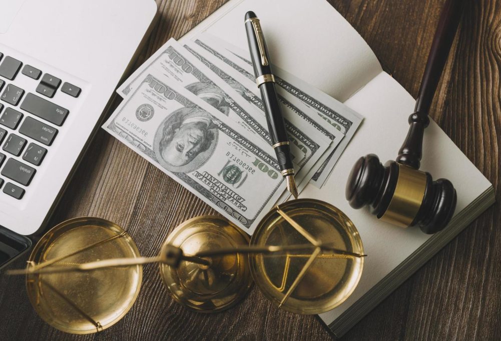 Symbolic representation of due process with money, a pen, and a scale of justice on a wooden table